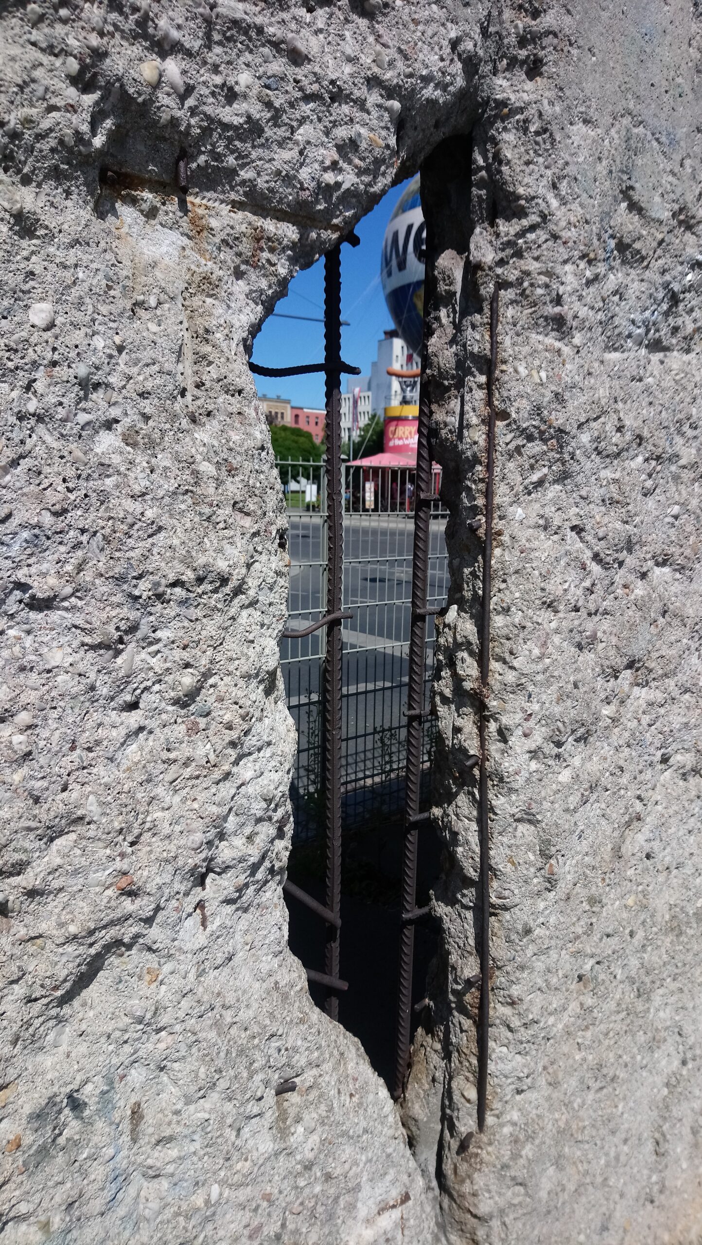 A hole in the Berlin Wall revealing buildings, blue sky, and a big balloon, symbolizing breaking through limits and testing online business ideas.