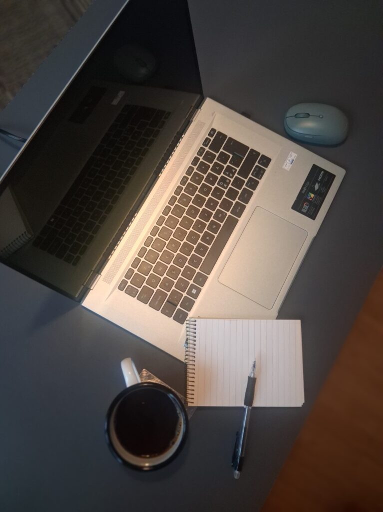 Laptop, notebook, pen and coffee on a desk used for writing and publishing work online.