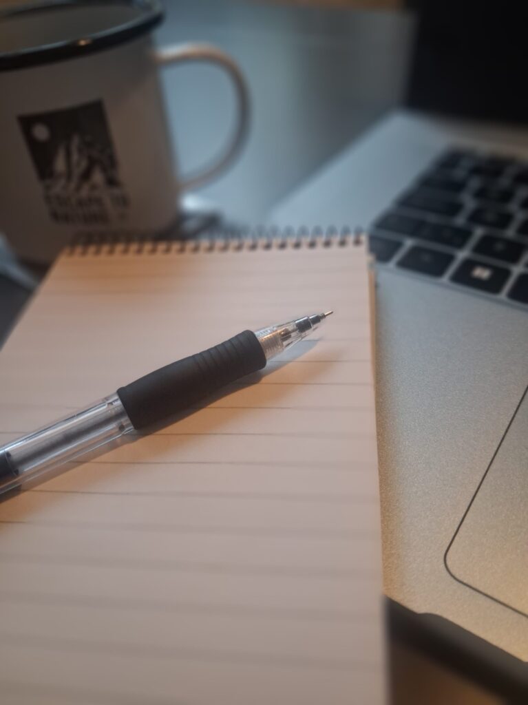 Laptop and notebook on desk, illustrating how to write better with AI using both technology and human input.