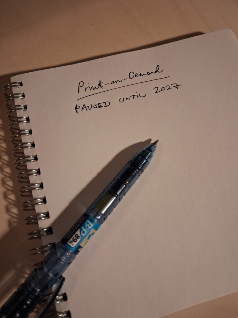 Notebook with handwritten note ‘Print-on-Demand paused until 2027’ representing closing open decisions.