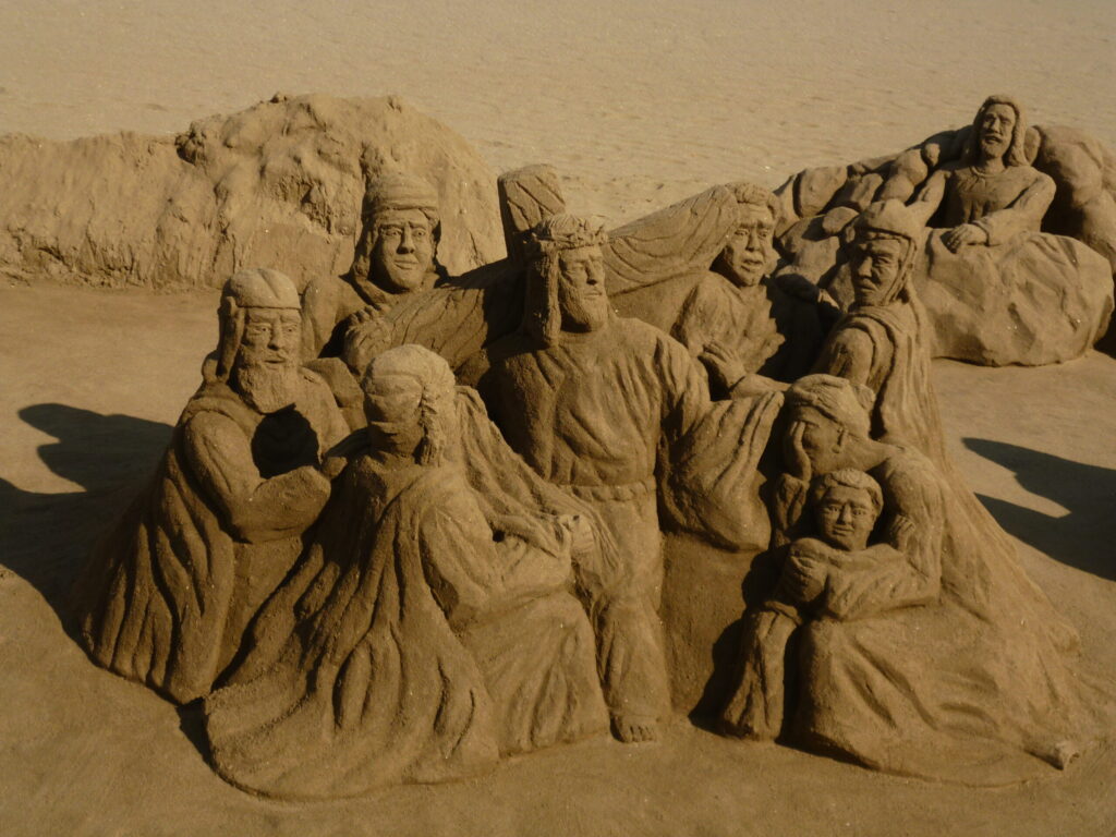 Large sand sculpture showing a group of historical and biblical figures carved in sand on a beach.