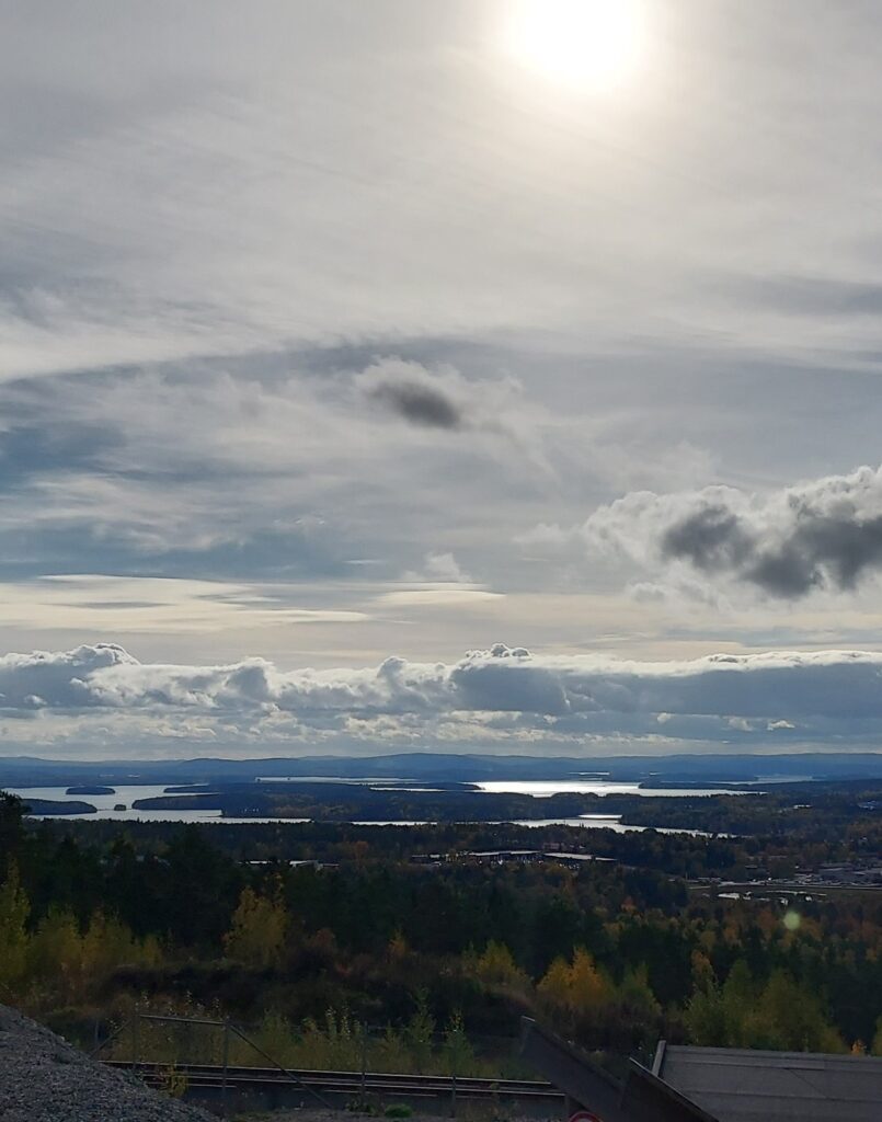 A wide landscape of forests, water and distant hills beneath a dramatic cloudy sky